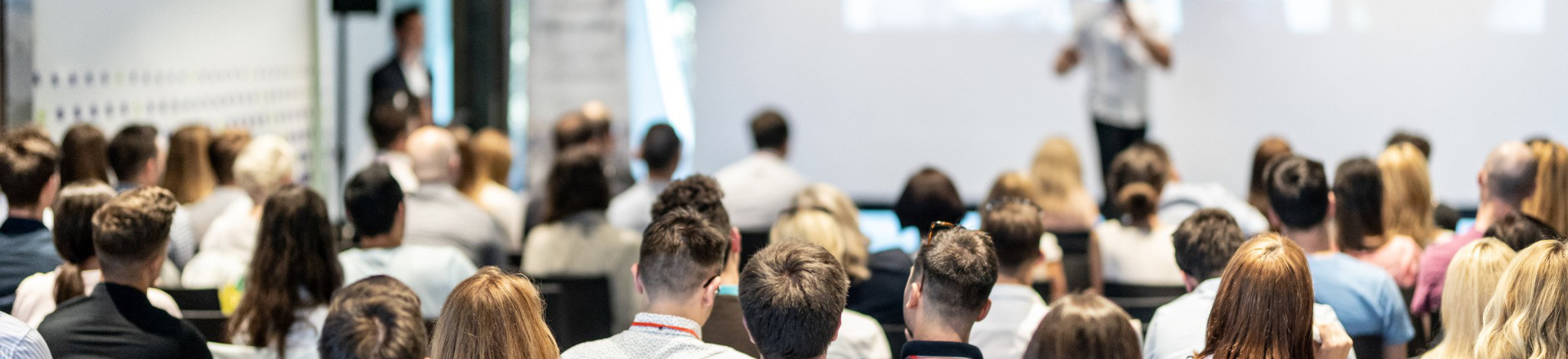 Team offsite session with a large audience seated indoors and listening to a speaker at the front of the room.