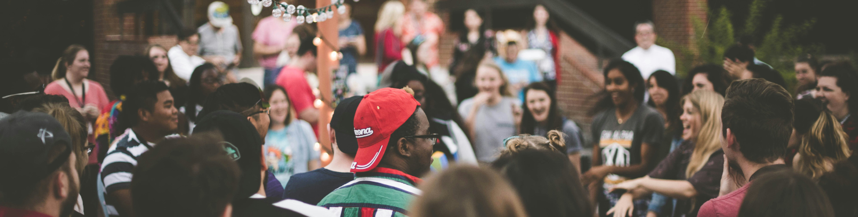 Large group of people standing in a circle outdoors, talking and laughing during a company retreat activity.