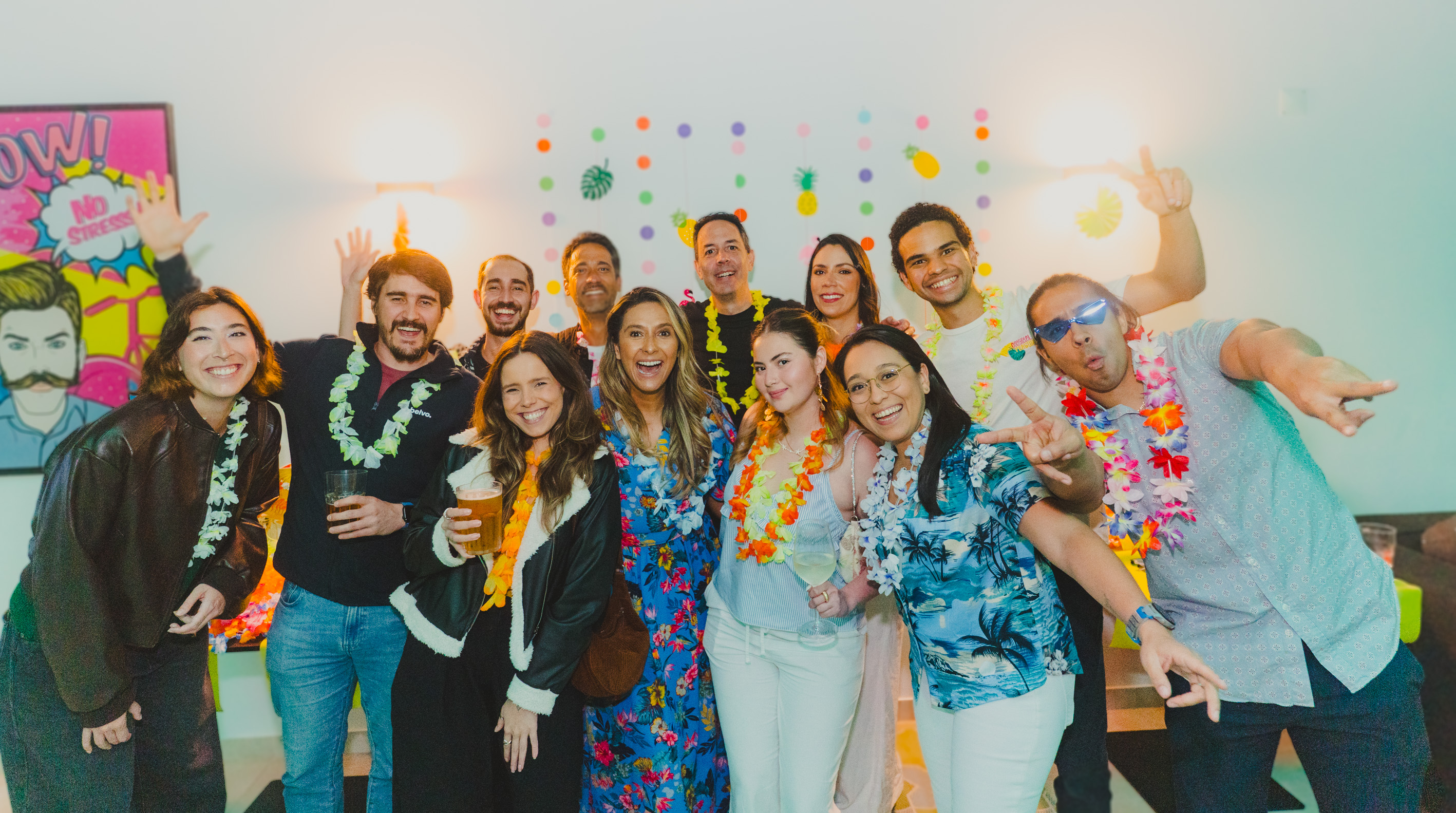 Group of colleagues in colourful leis smiling and posing together at an indoor celebration, illustrating the social side of high-performing teams.
