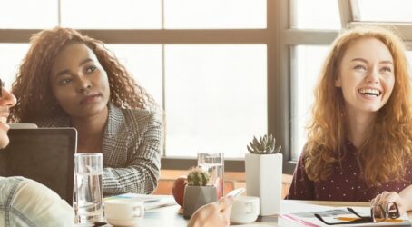 Team offsite planning discussion with a small group of colleagues gathered around a table in a bright meeting space, smiling and engaged in conversation while reviewing ideas and notes during an informal strategy session.