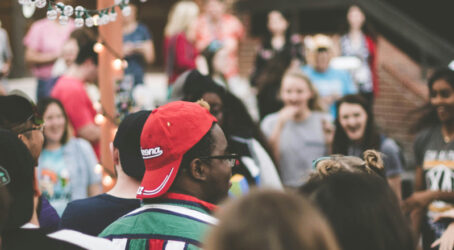 Large group of people standing in a circle outdoors, talking and laughing during a company retreat activity.