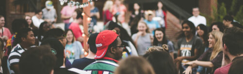 Large group of people standing in a circle outdoors, talking and laughing during a company retreat activity.