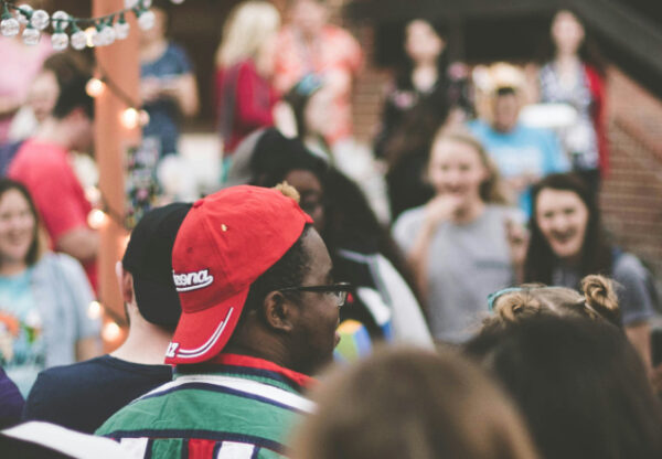 Large group of people standing in a circle outdoors, talking and laughing during a company retreat activity.