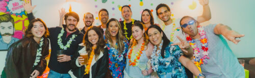 Group of colleagues in colourful leis smiling and posing together at an indoor celebration, illustrating the social side of high-performing teams.