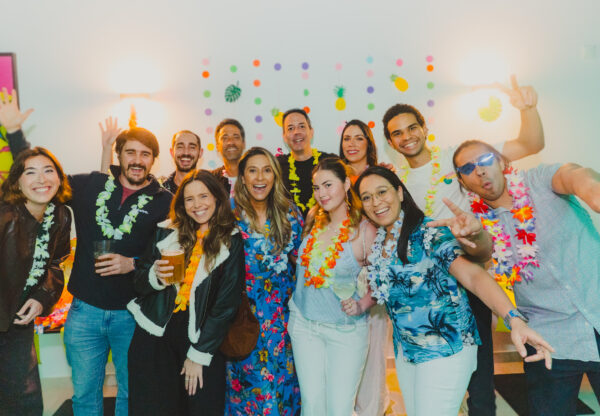 Group of colleagues in colourful leis smiling and posing together at an indoor celebration, illustrating the social side of high-performing teams.