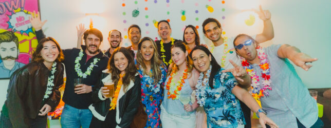 Group of colleagues in colourful leis smiling and posing together at an indoor celebration, illustrating the social side of high-performing teams.