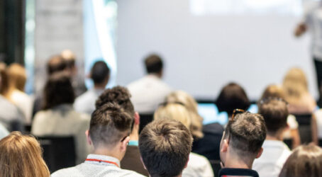 Team offsite session with a large audience seated indoors and listening to a speaker at the front of the room.