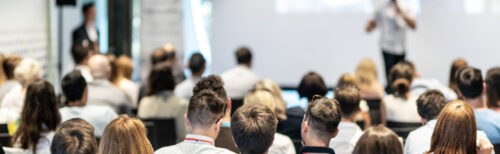 Team offsite session with a large audience seated indoors and listening to a speaker at the front of the room.