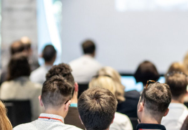 Team offsite session with a large audience seated indoors and listening to a speaker at the front of the room.