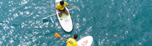 Two employees paddleboarding on clear blue water during a company retreat team-building activity and outdoor corporate getaway.