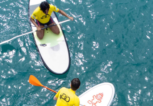 Two employees paddleboarding on clear blue water during a company retreat team-building activity and outdoor corporate getaway.